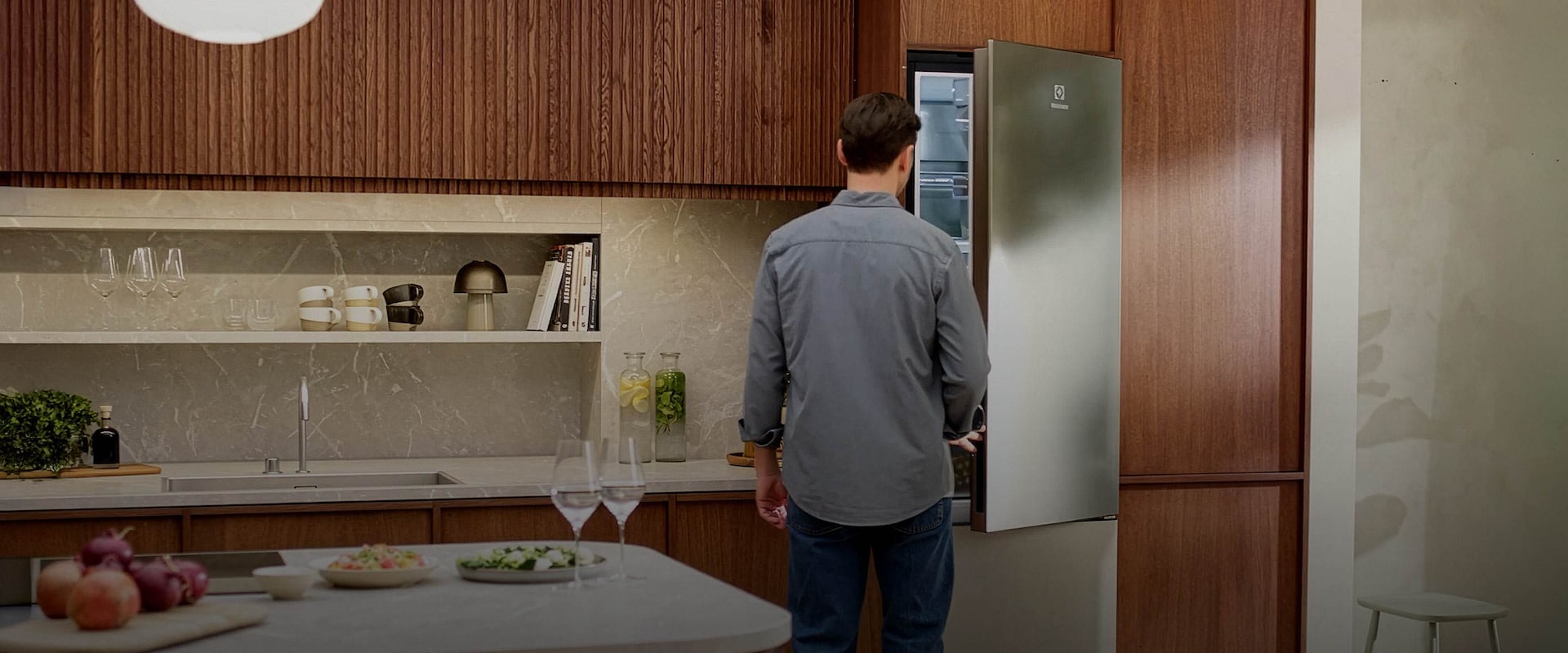 En mann åpner et frittstående kombiskap i rustfritt stål-look fra Electrolux